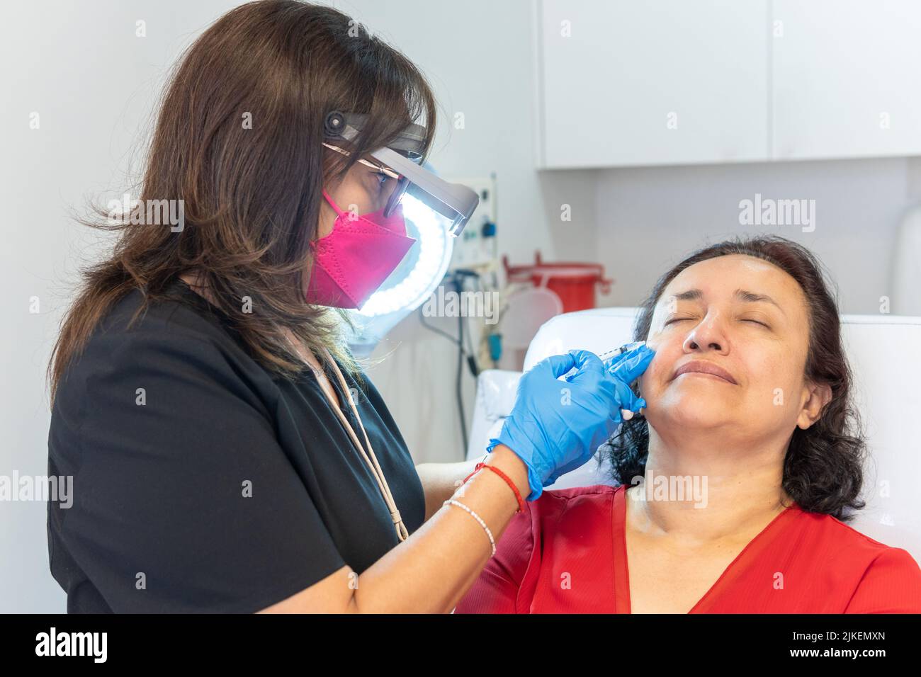 Frau, die Hyaluronsäure-Füllstoff neben ihren Augen erhält, um Falten zu entfernen. Ärztin injiziert mit einer Spritze in einem ästhetischen Zentrum, echte Menschen Stockfoto