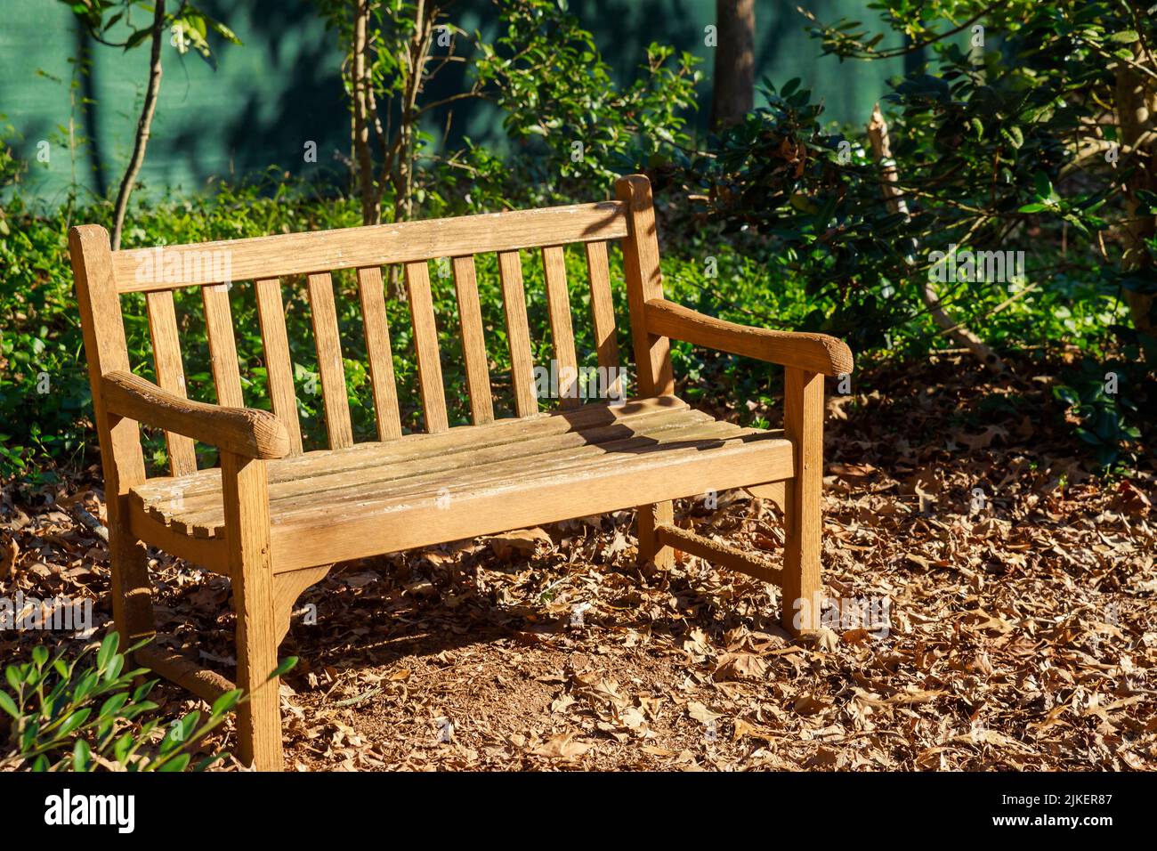 Eine leere Holzbank in einem Park mit trockenen Blättern. Stockfoto