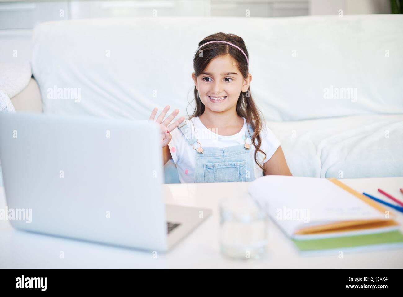 Lächle einfach und winke. Ein kleines Mädchen, das zu Hause einen Laptop benutzt. Stockfoto