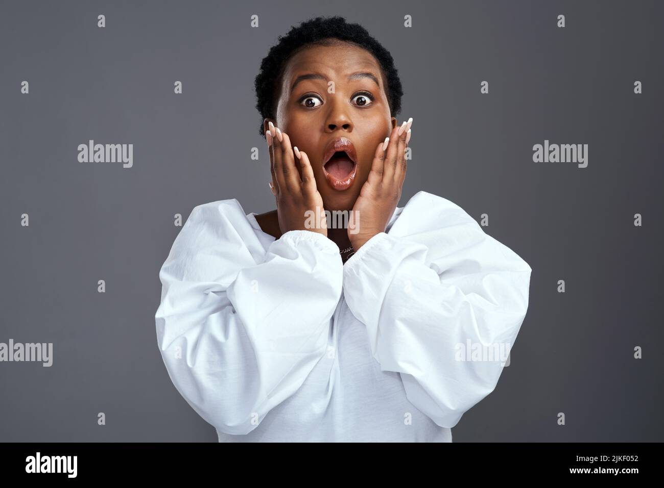 Haben Sie gehört? Eine Frau, die schockiert aussieht, während sie vor einem grauen Hintergrund steht. Stockfoto