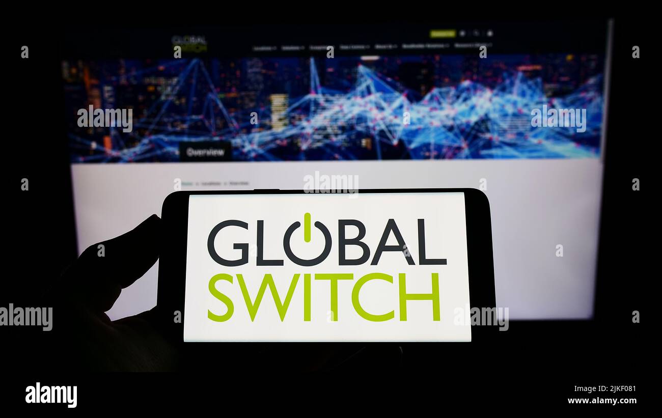 Person, die das Smartphone mit dem Logo des britischen Rechenzentrumsunternehmens Global Switch Limited auf dem Bildschirm vor der Website hält. Konzentrieren Sie sich auf die Telefonanzeige. Stockfoto
