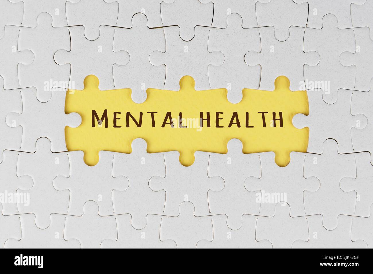 Weißes Puzzle mit Text auf drei fehlenden Teilen auf weichem Gelb. Psychische Gesundheit. Heilung und Beratung. Selbstliebe und Fürsorge. Psychische Erkrankungen. Stockfoto