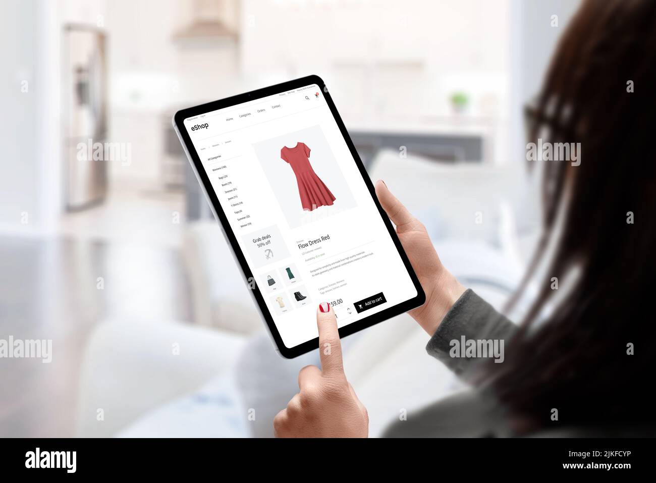 Frau kauft online ein Kleid mit Tablet-Konzept. Moderne E-Commerce-Bekleidungs-Website. Wohnzimmer im Hintergrund Stockfoto