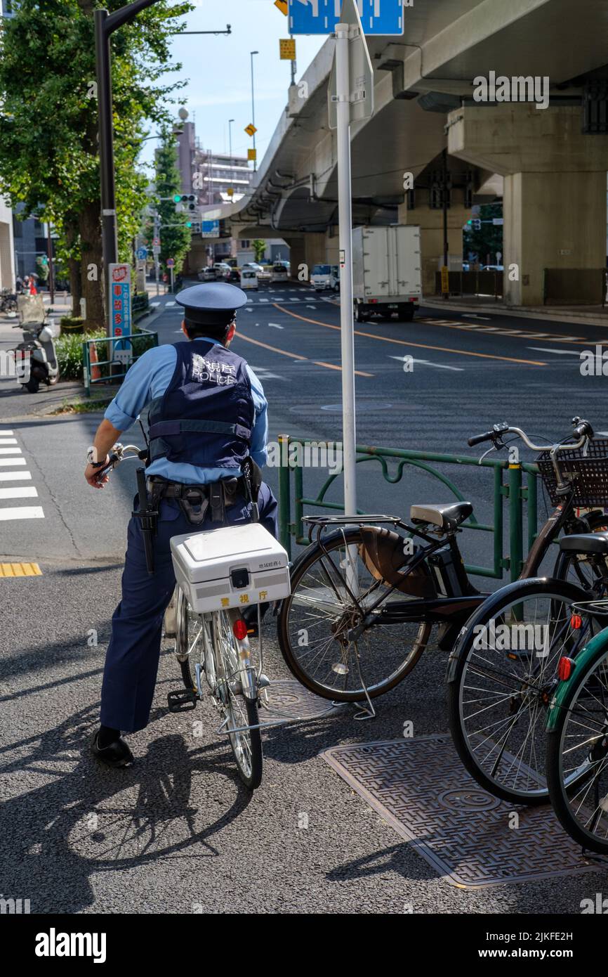 TOKIO, JAPAN - 10. AUGUST 2019: Polizeibeamter auf einem Fahrrad blickt an einem heißen Sommertag in Tokio, Japan, am 10. August 2019 auf eine Kreuzung. Stockfoto