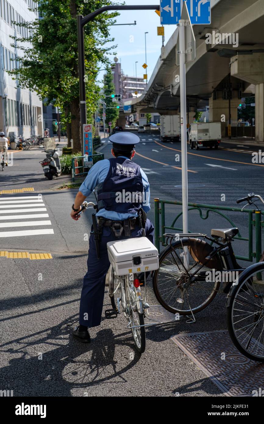 TOKIO, JAPAN - 10. AUGUST 2019: Polizeibeamter auf einem Fahrrad blickt an einem heißen Sommertag in Tokio, Japan, am 10. August 2019 auf eine Kreuzung. Stockfoto