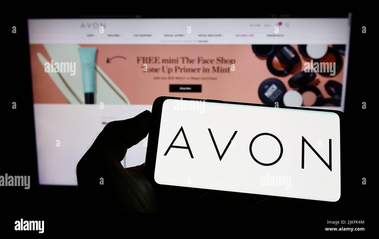Person mit Mobiltelefon und Logo des Kosmetikunternehmens Avon Products Inc. Auf dem Bildschirm vor der Business-Webseite. Konzentrieren Sie sich auf die Telefonanzeige. Stockfoto