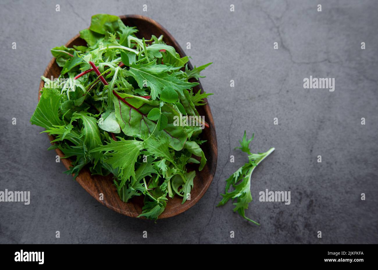 Mischung aus frischen grünen Salatblättern mit Rucola und Rüben auf dem Teller auf dunklem Betongrund. Zutat für gesunde Salate Stockfoto