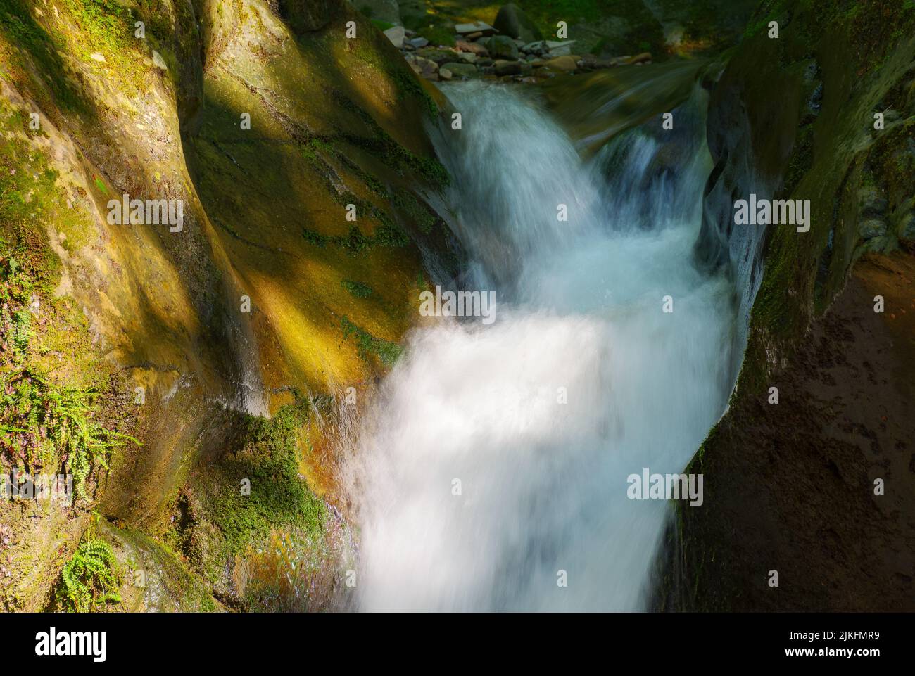 Dünner, aber kraftvoller Wasserfall zwischen den Felsbrocken. Erfrischender Sommer Natur Hintergrund im Wald Stockfoto