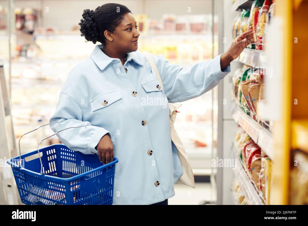 Seitenansicht Porträt einer jungen schwarzen Frau, die Lebensmittel im Supermarkt kauft und Pasta wählt Stockfoto
