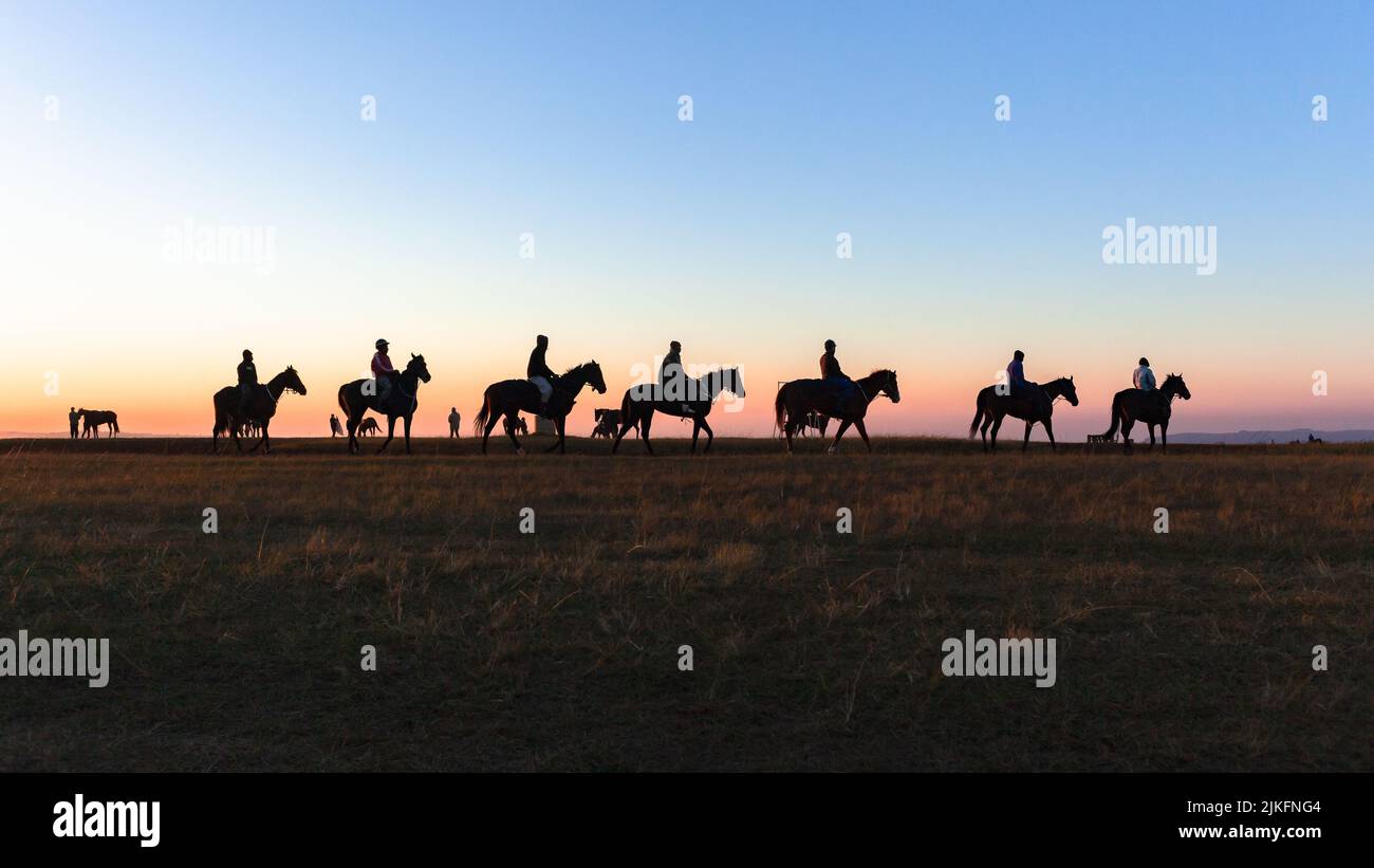 Rennpferde dämmern silhoutted Tiere Reiter wärmen Trainingspfad mit blauen Himmel Horizont Farben eine malerische Landschaft. Stockfoto