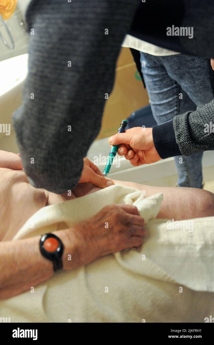 Private Krankenschwester, die während der Toilette einen Bluttest und eine Insulinininjektion an einem 87-jährigen Patienten durchführt. Die Patientin ist mit einem Armband für Fernalarm am Handgelenk ausgestattet. Stockfoto