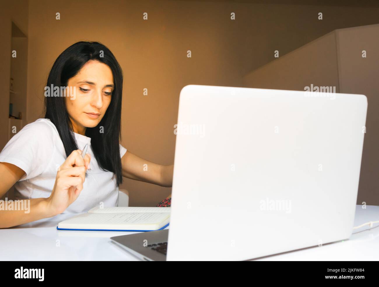 Eine junge, langhaarige georgische Frau mit dunklen Haaren notiert sich in ihrem Wohnzimmer Stockfoto