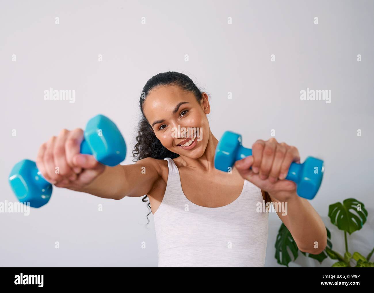 Eine junge Frau lächelt, während sie zu Hause 2kg Gewichte hält Stockfoto