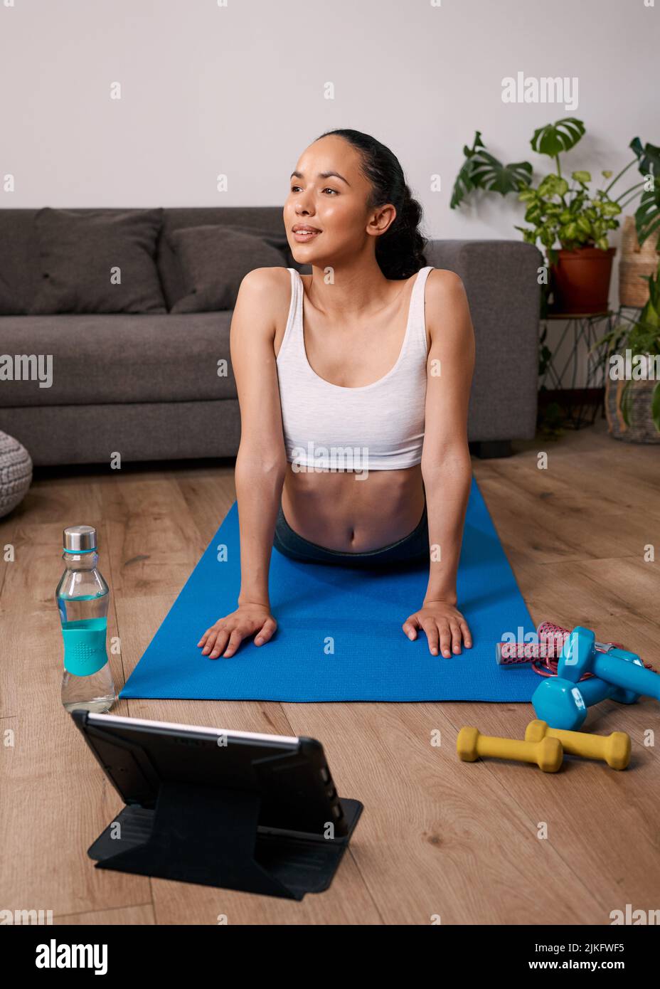 Eine junge Frau streckt sich während des virtuellen Heimtrainings in einen nach oben schauenden Hund Stockfoto