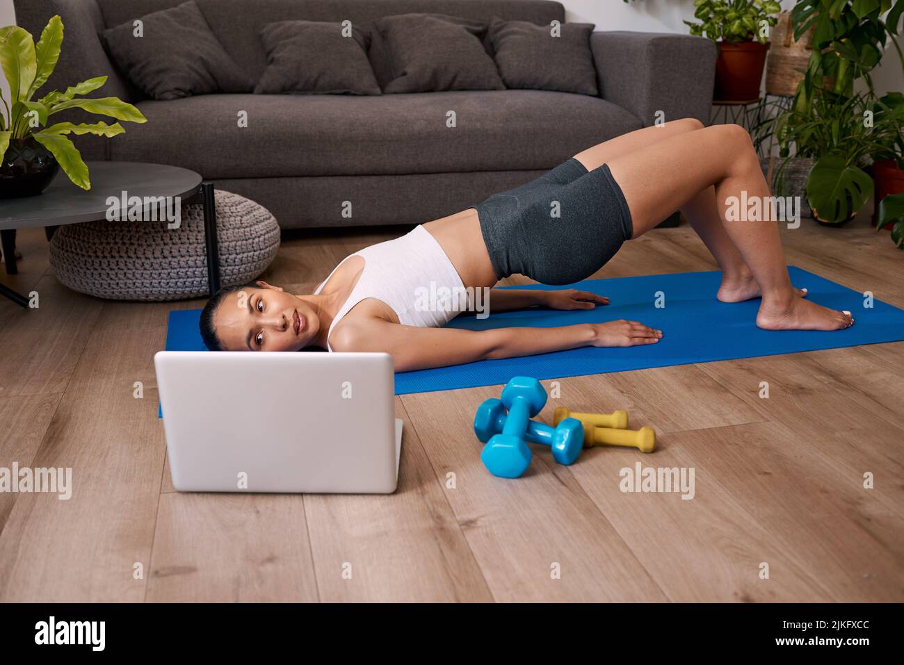 Junge multiethnische Frau macht Bridge-Übung beobachten Online-Fitness-Klasse Stockfoto