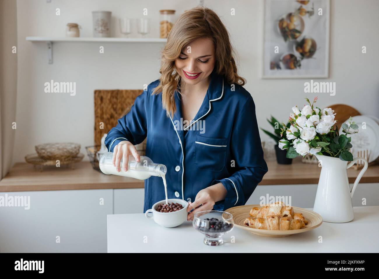 Schönes Mädchen gießt Müsli mit Milch in der Küche Stockfoto