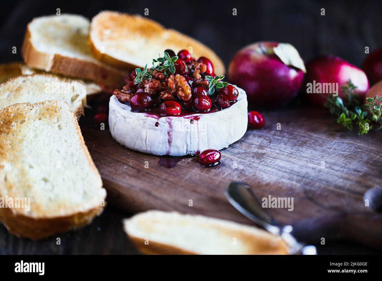 Gebackenen Camembert Brie Käse mit Cranberry, Honig, Balsamico-Essig und Nuss genießen und mit Thymian garniert. Serviert mit gerösteten Brotscheiben. Stockfoto