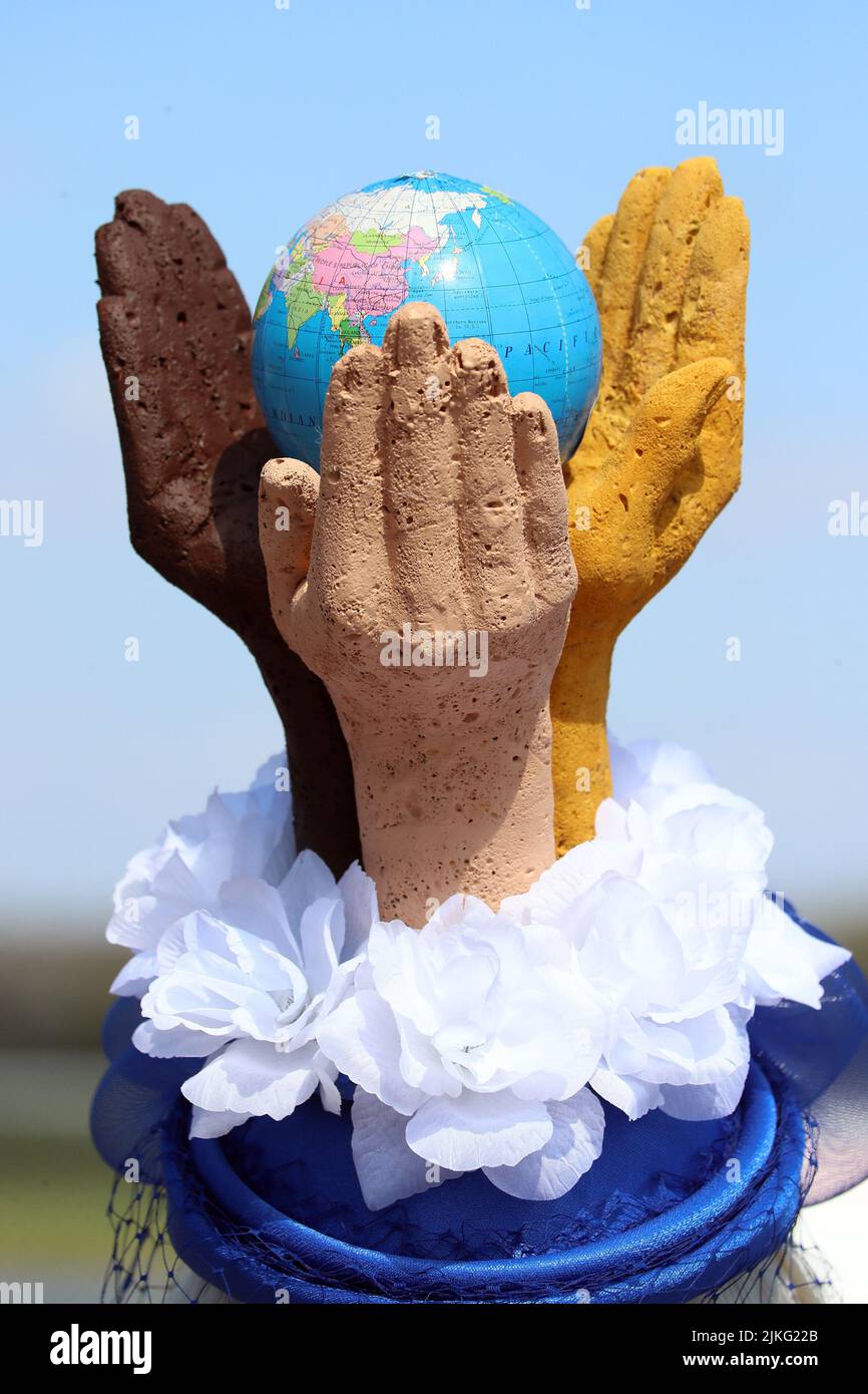 23.04.2022, Deutschland, Sachsen-Anhalt, Magdeburg - Hutkreation: Hände verschiedener Hautfarben umarmen einen Globus. 00S220423D365CAROEX.JPG [MODELLVERSION: Stockfoto