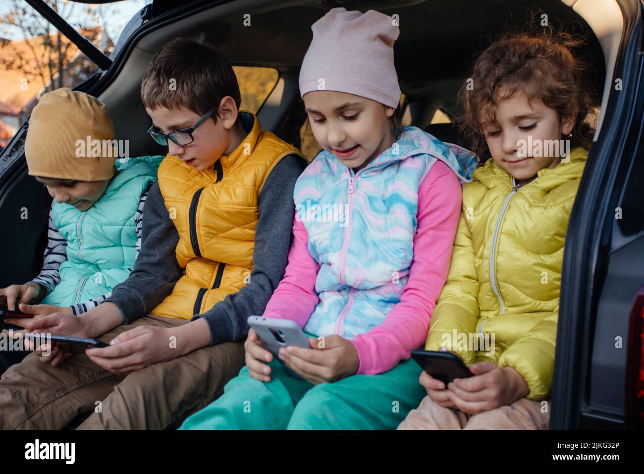 Kinder sitzen mit Smartphones auf dem Autotruck und haben Spaß Stockfoto
