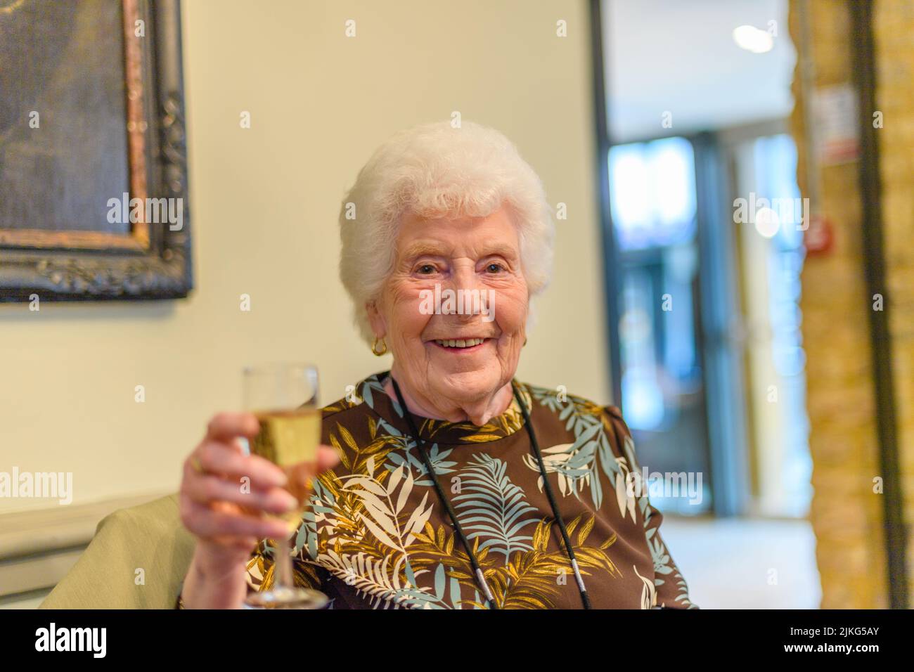 Eine fröhliche alte kaukasische Frau, die ein Glas Wein hält, um zu feiern Stockfoto
