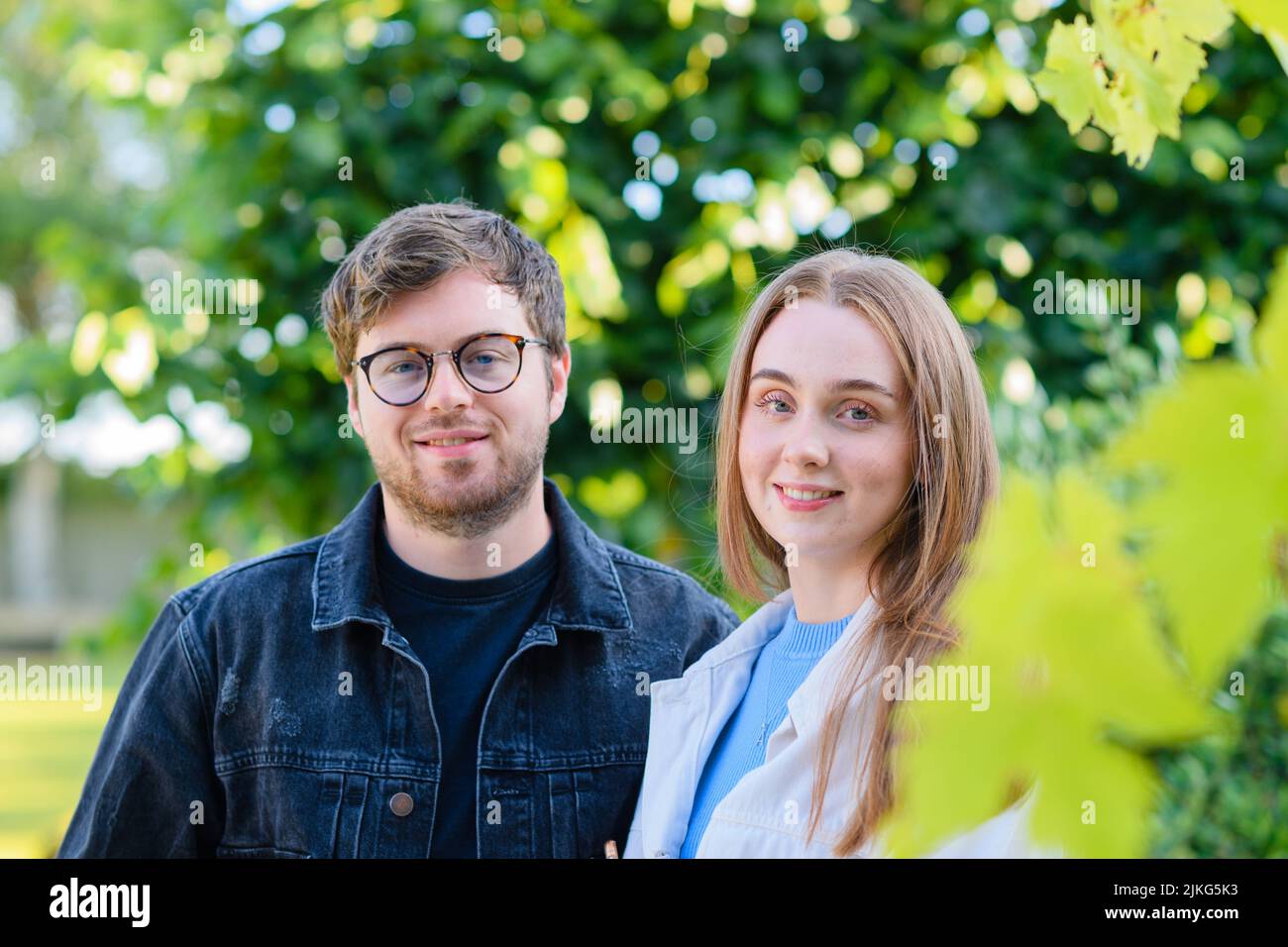 Ein Porträt eines glücklichen kaukasischen Paares, das vor den grünen Bäumen posiert Stockfoto