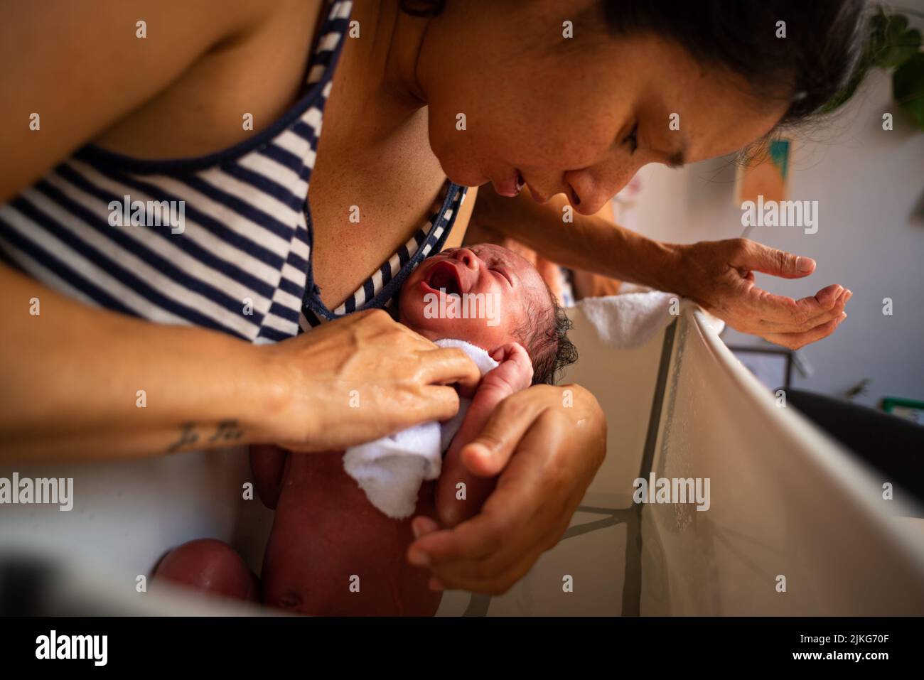 Junge Mutter tut erstes Bad zu neugeborenen Tochter zu Hause. Szene der Intimität und Pflege für die Familie und Konzept der Mutterschaft. Stockfoto