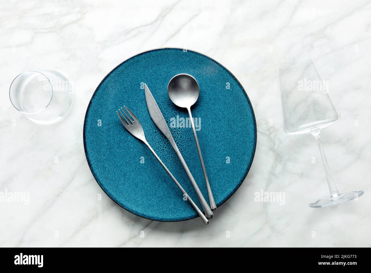 Modernes Geschirr mit blauem Teller, Besteck und Gläsern, von oben geschossen. Eleganter Dinner-Service auf einem weißen Marmortisch Stockfoto
