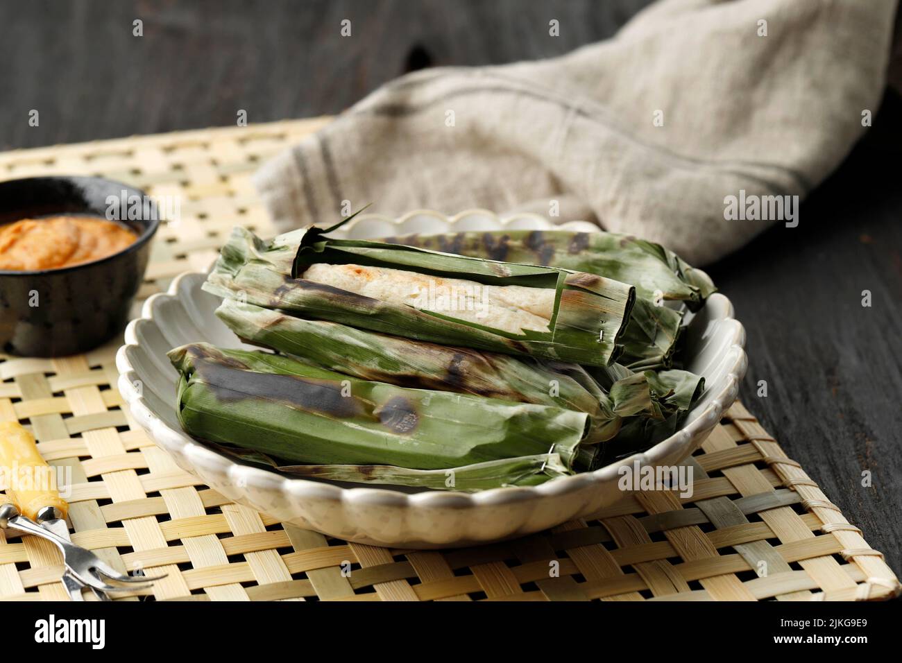 Gegrillter Otak-Otak, indonesischer Fischkuchen, eingewickelt mit Bananenblatt und Grill. Serviert mit Erdnusssauce oder süßer und herzhafter roter würziger Sauce Stockfoto