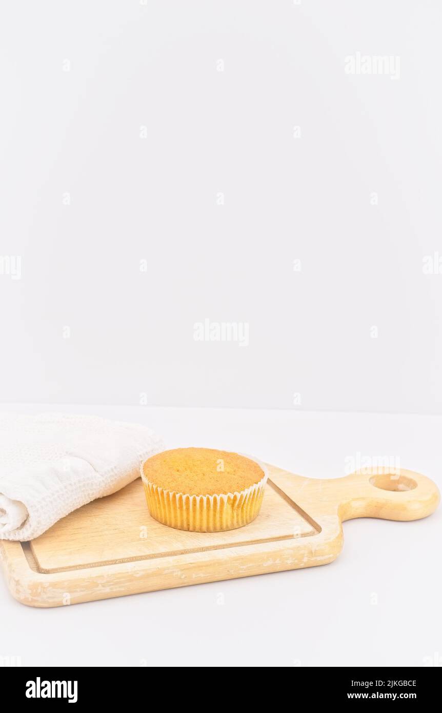 Karottenkuchen aus biologischem Anbau in einem Papierbecher mit Dinkelmehl, Küchentuch und Holzschneidebrett auf einem weißen Tisch Stockfoto