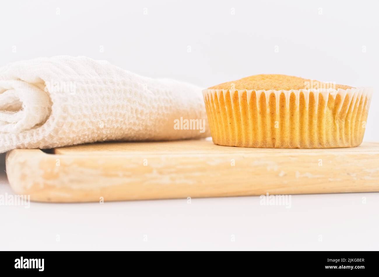 Karottenkuchen aus biologischem Anbau in einem Papierbecher mit Dinkelmehl, Küchentuch und Holzschneidebrett auf einem weißen Tisch Stockfoto