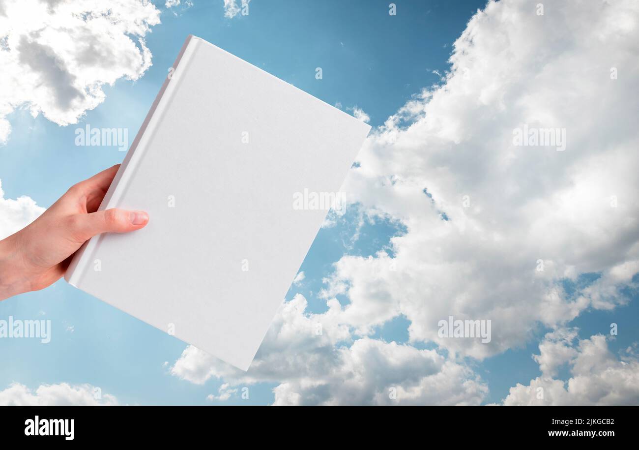 Hand mit Buchmockup auf blauem bewölktem Himmel Hintergrund. Bibel, inspirierendes Literaturkonzept. Hochwertige Fotos Stockfoto