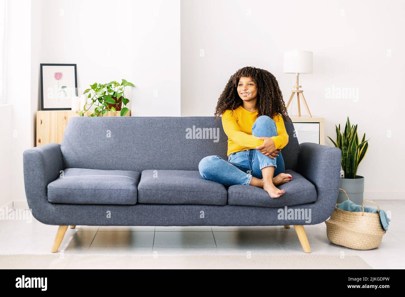 Entspannt lächelnde afroamerikanische Frau, die zu Hause auf dem Sofa sitzt Stockfoto