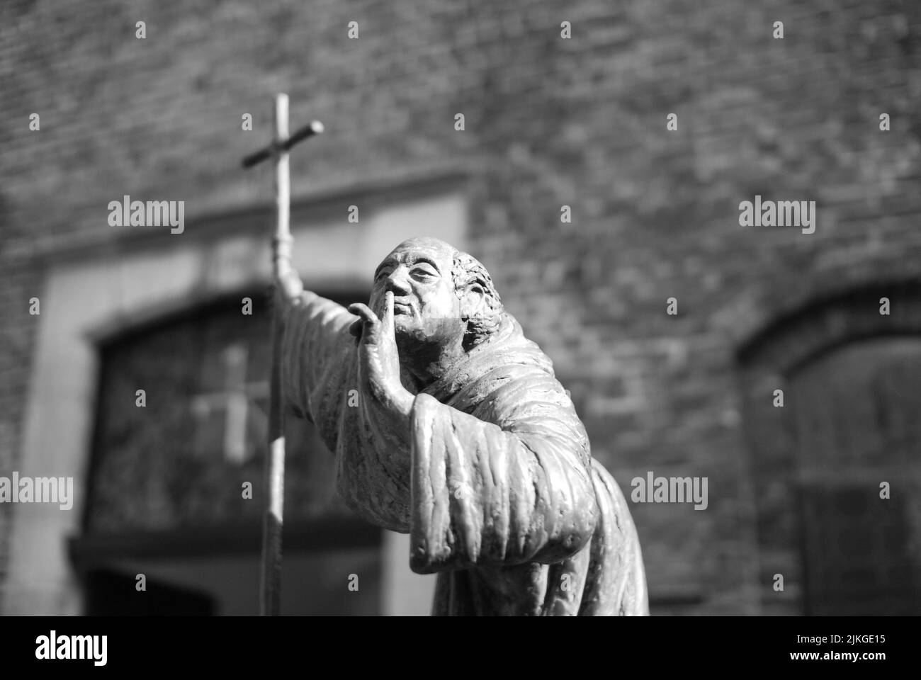 Eine Bronzeskulptur eines stillen Mönchs mit einem Kreuz in der Hand in Venlo, Niederlande Stockfoto