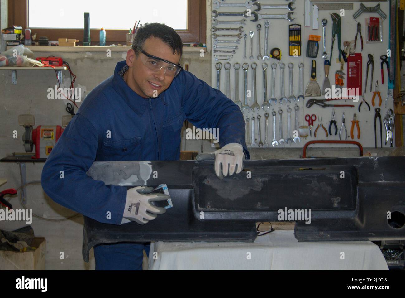 Bild eines lächelnden Karosseriebauers, der einen Autostoßfänger schleift und repariert. Do-it-yourself-Arbeit Stockfoto