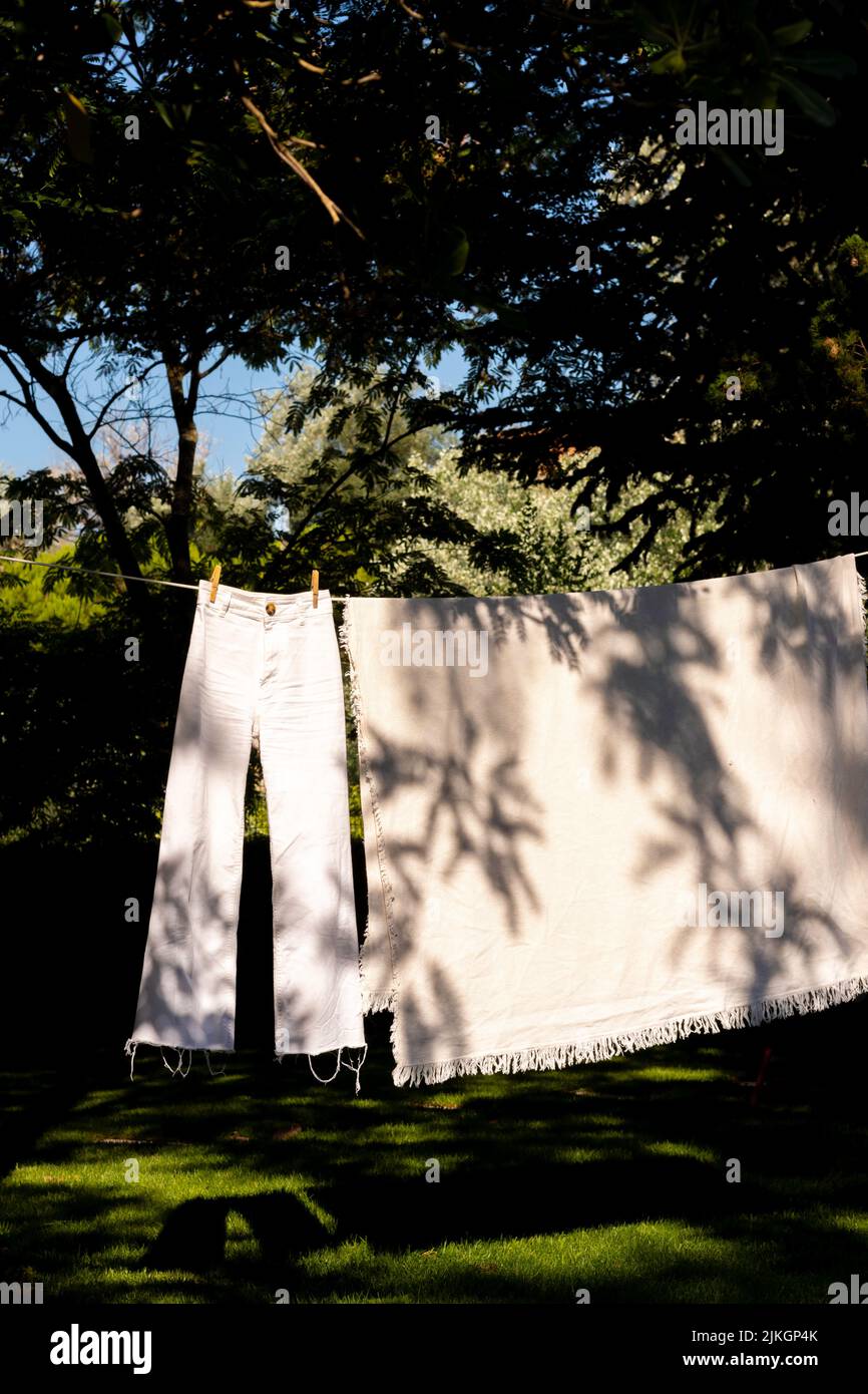 Aufhängen einer Hose und Leinenkleidung in einer Wäscheleine im Garten mit Pflanzenschatten auf ihnen und natürlichem Boho-Stil Stockfoto