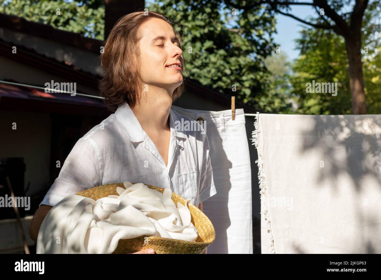 Porträt eines jungen Mannes, der im Garten Hausarbeiten als Wäsche macht, mit geschlossenen Augen und der Sonne im Sommer im Gesicht Stockfoto