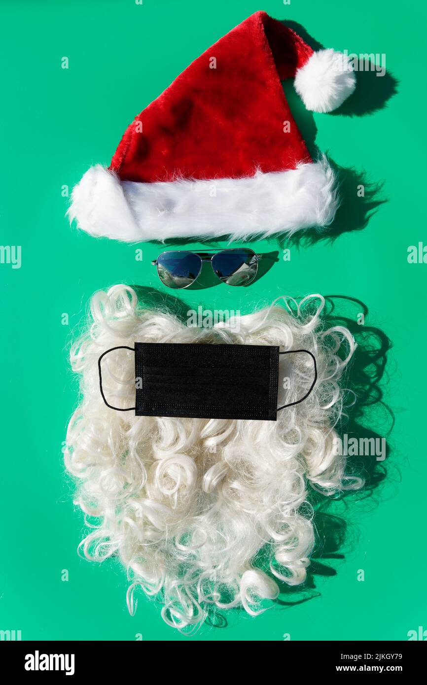 weihnachtsmann mit Sonnenbrille in schützender covid-19 Gesichtsmaske auf grünem Hintergrund Stockfoto