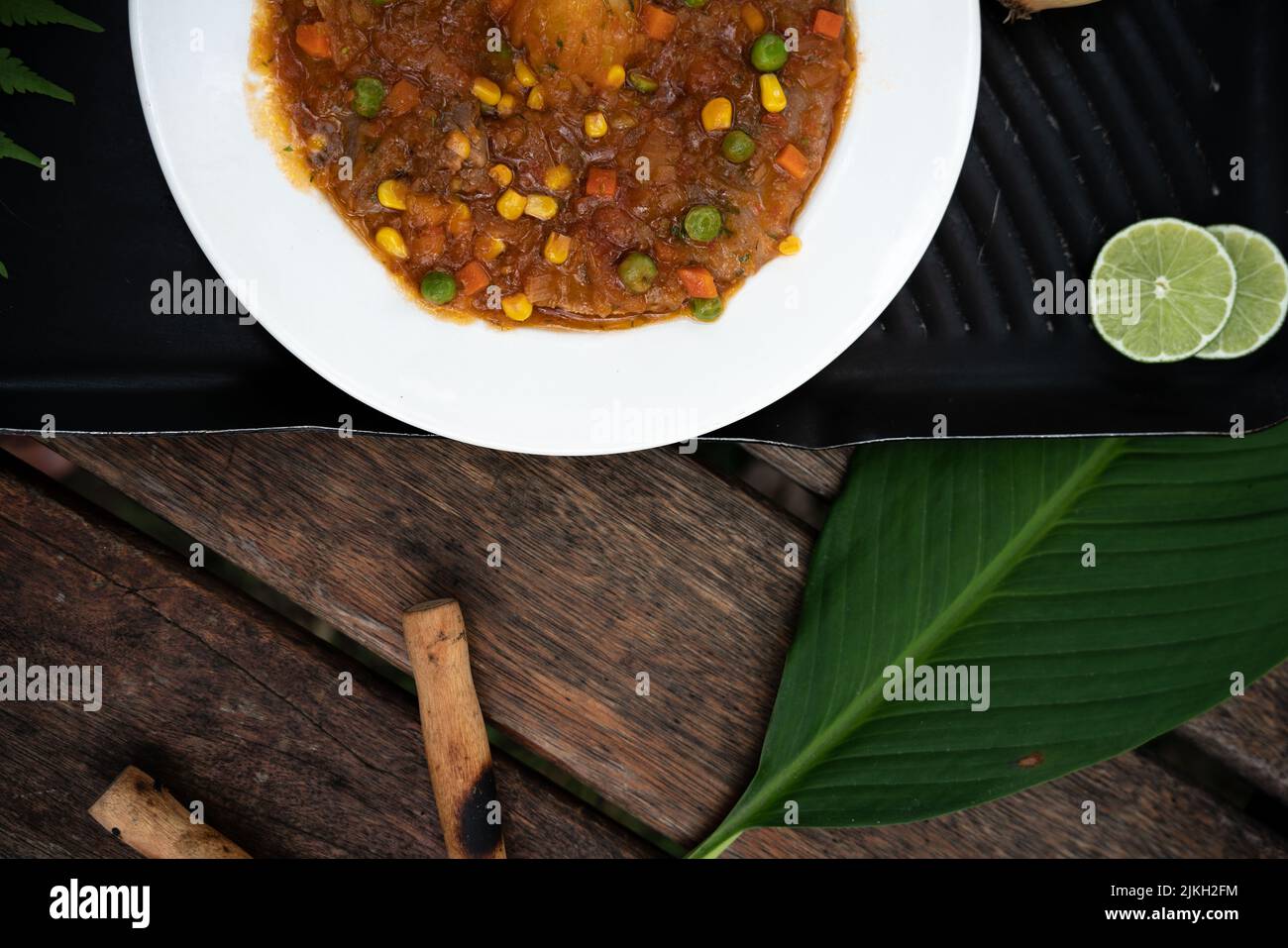 Eine Draufsicht auf eine Schüssel Gemüseeintopf mit Mais und Erbsen auf einem Holztisch Stockfoto