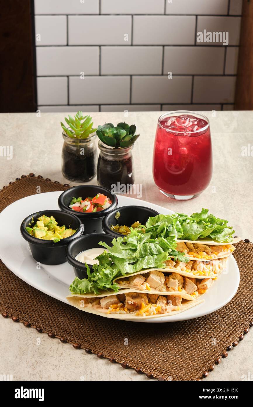 Eine vertikale Nahaufnahme von Quesadillas, serviert mit einem Getränk und Saucen Stockfoto