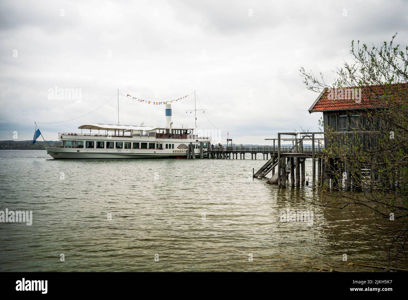 Ein traditionelles Bootshaus und ein Touristenschiff auf dem Ammersee bei München, Bayern, Deutschland Stockfoto