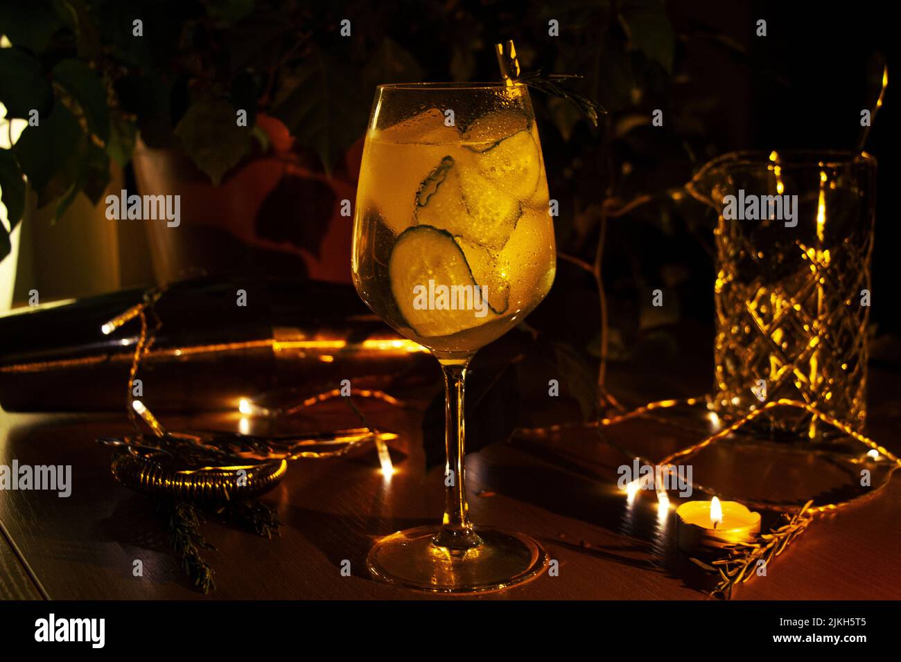 Eine Nahaufnahme eines Gin Tonic-Cocktails aus Gurken in einem Weinglas, das mit Kerzen und Lichtern dekoriert ist Stockfoto