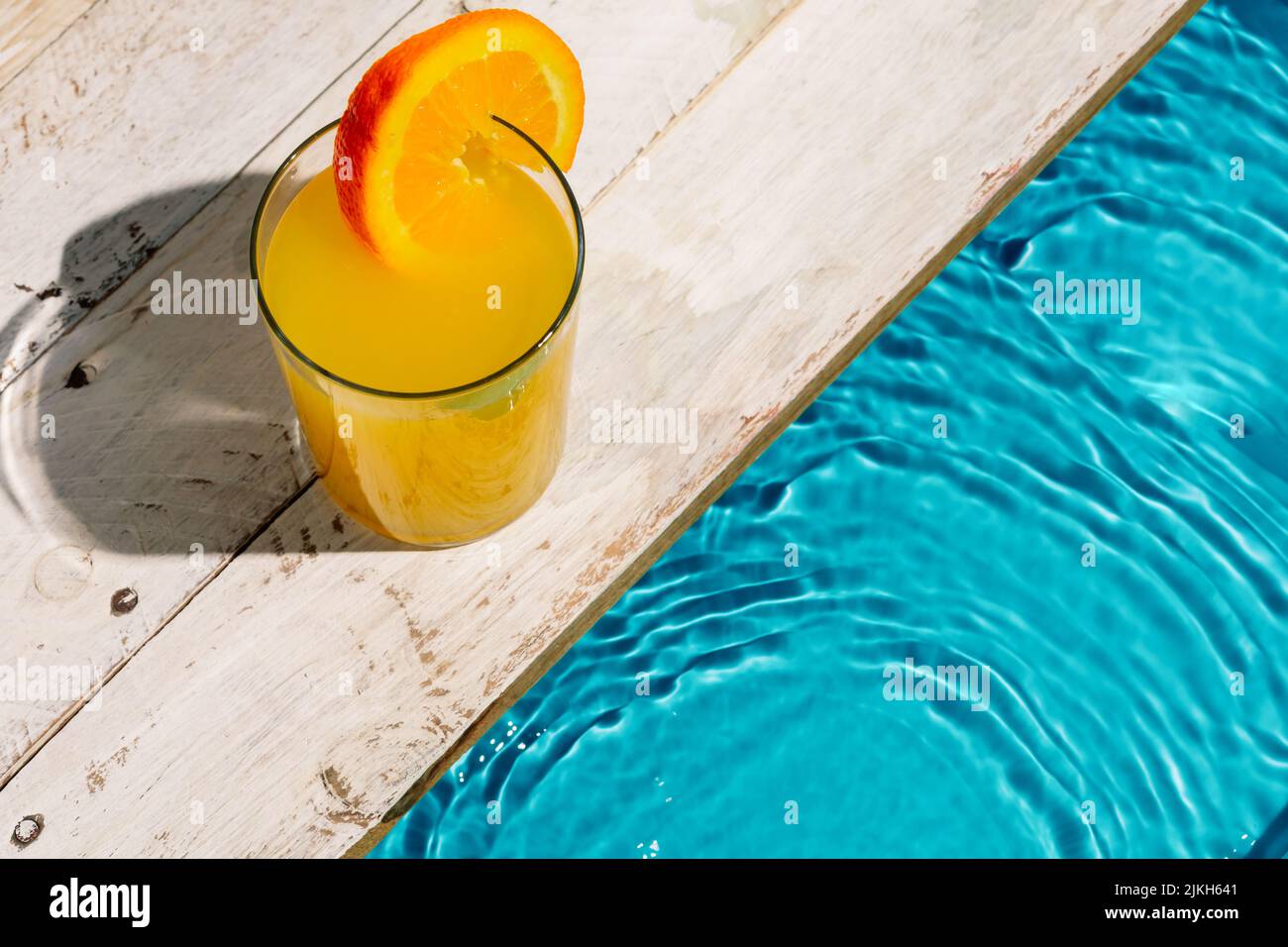Eine Tasse Orangensaft mit Orangenscheibe neben dem Pool Stockfoto
