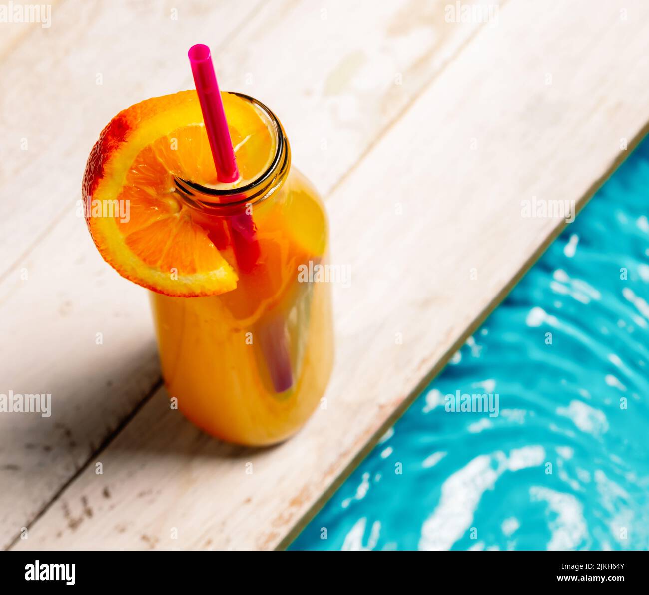 Eine Tasse Orangensaft mit Orangenscheibe und Stroh neben dem Pool Stockfoto