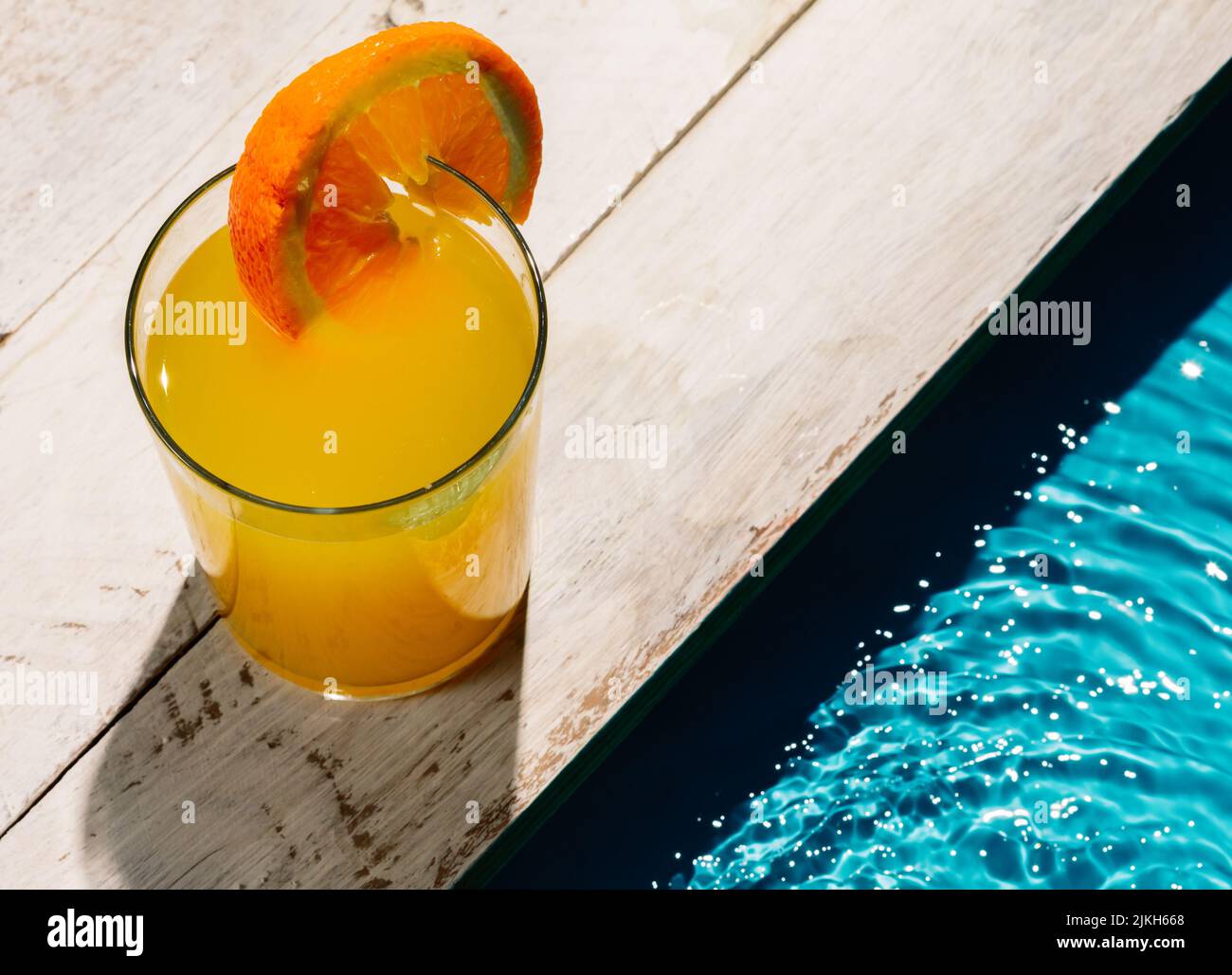 Eine Tasse Orangensaft mit Orangenscheibe neben dem Pool Stockfoto