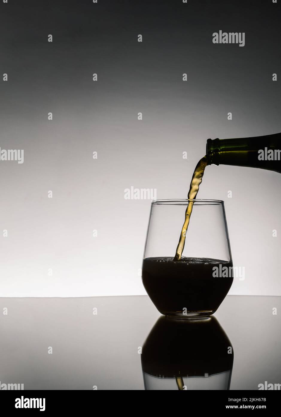 Das Bier wurde aus der Flasche, die auf dem Tisch auf dunklem Grund gespiegelt war, in ein Glas gegossen Stockfoto