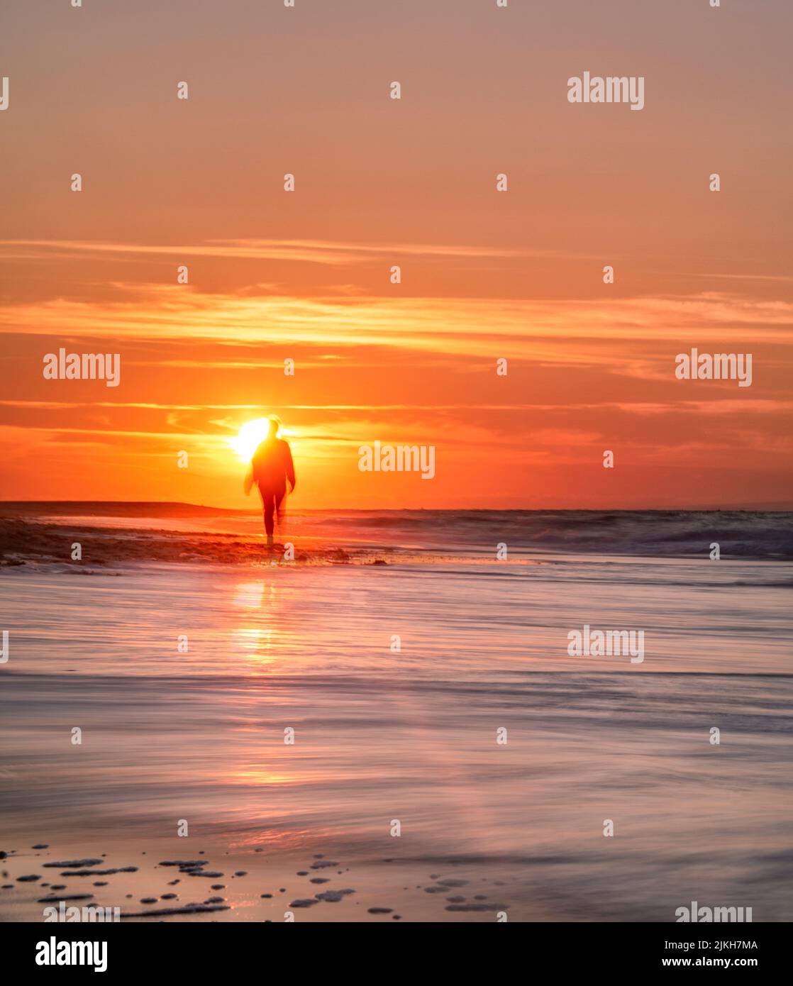 Ein Langzeitfoto eines Strandes bei Sonnenuntergang mit der Silhouette eines Laufers Stockfoto