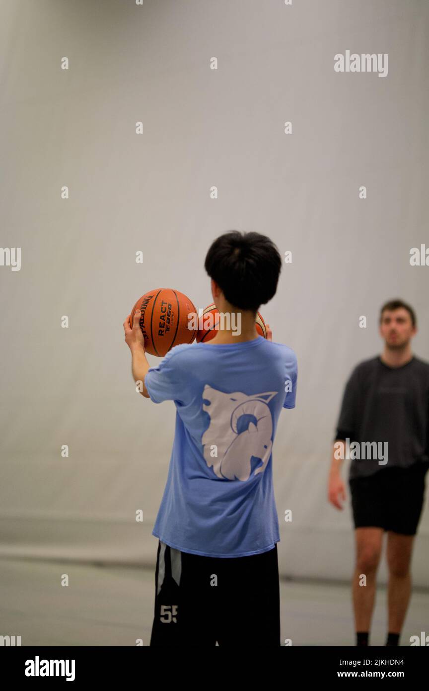 Eine vertikale Aufnahme eines Asiaten, der Basketbälle vergleicht Stockfoto