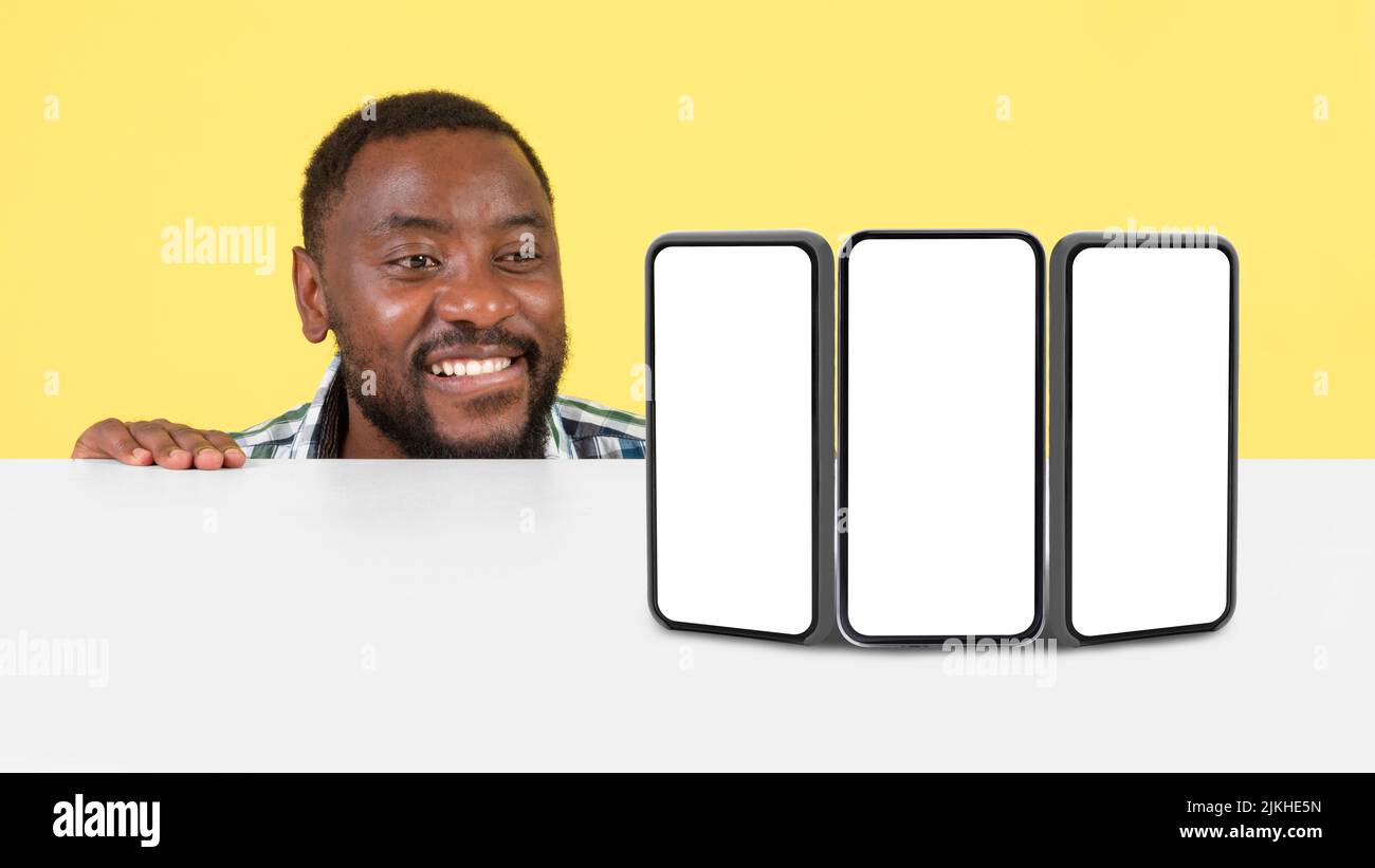 Schwarzer Mann Mit Blick Auf Drei Handys Leere Bildschirme, Gelber Hintergrund Stockfoto