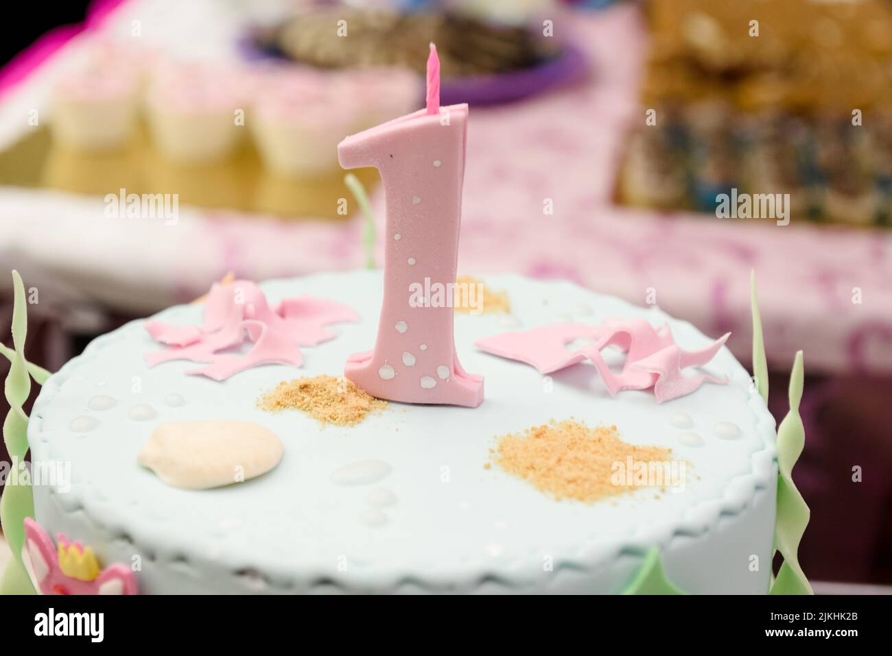Eine festliche Torte mit einer rosa Marzipan-Nummer und einer kleinen Kerze für einen ersten Geburtstag oder ein Jubiläum auf einem verschwommenen Hintergrund Stockfoto
