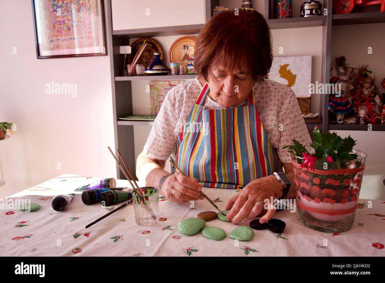 Eine reife kaukasische Frau, die zu Hause in Barcelona, Spanien, Steine mit Acrylfarben auf den Tisch malt Stockfoto